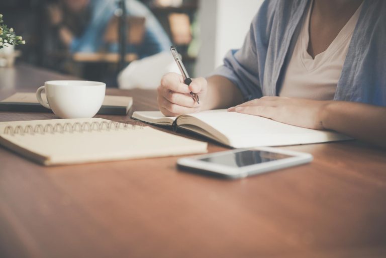 woman writing on a notebook beside teacup and tablet computer make money blogging